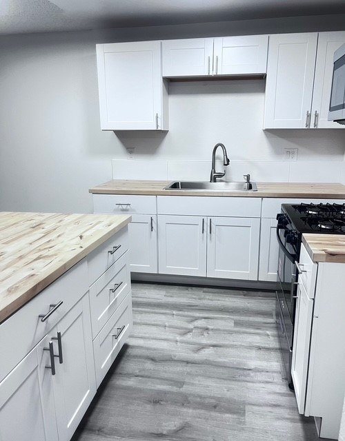 A kitchen with white cabinets and a wooden counter top.